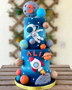 a three tiered blue cake with an astronaut on top and planets around the base