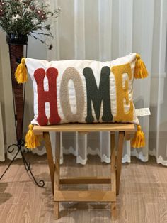 a decorative pillow with the word home on it sitting on a stool in front of a window