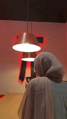 a person in a hooded jacket looking at a cell phone under a light hanging from the ceiling