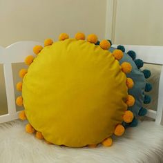 a yellow pillow with pom - poms sitting on top of a white chair