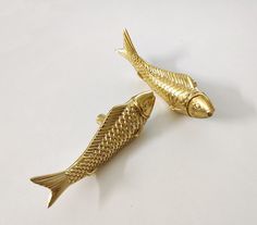 two gold fish shaped brooches on a white surface