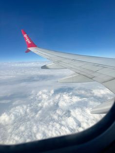 the wing of an airplane flying high above the clouds and blue sky with bright red letters on it