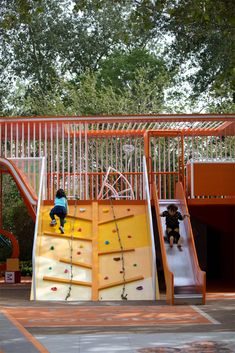 two children are climbing up and down a slide at a playground with trees in the background