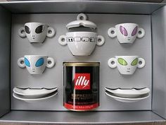 an open box with coffee cups and saucers on the inside, in which there are alien heads