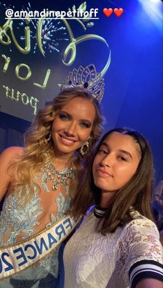 two beautiful young women standing next to each other in front of a blue stage backdrop