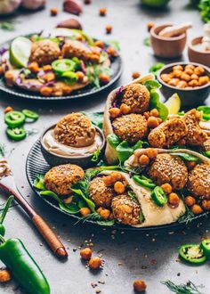 two plates filled with food on top of a table next to bowls of vegetables and sauces