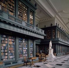 an old library filled with lots of books and tables next to a statue in the middle