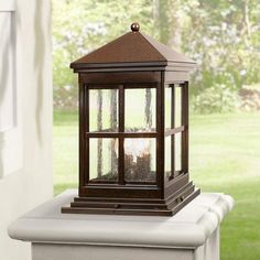 an outdoor lantern is sitting on the ledge in front of a window with grass and trees behind it