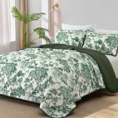 a green and white comforter set on top of a bed in front of a window