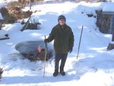 a man standing in the snow with skis and poles next to a fire pit