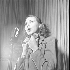 a black and white photo of a woman in front of a microphone talking on the phone