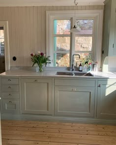 a kitchen with white walls and wooden floors has two windows that look out onto the yard