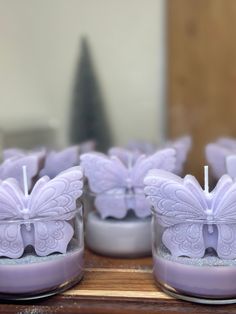 several candles with butterflies on them are sitting in glass containers, one is purple and the other is white