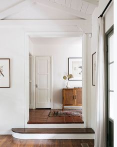 an entryway with wood floors and white walls, framed pictures on the wall above it