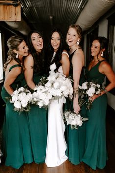 a group of women standing next to each other in green dresses holding bouquets and smiling