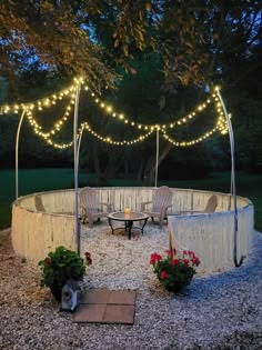 an outdoor seating area with lights strung over it and flowers in the foreground, surrounded by gravel