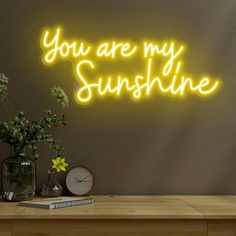 you are my sunshine neon sign with clock and flowers in vases on wooden table