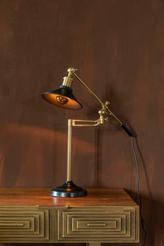 a desk lamp sitting on top of a wooden table in front of a brown wall