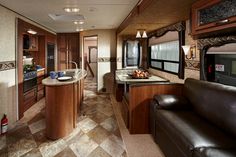 a kitchen and living room in an rv with wood cabinets, tile flooring and leather couches