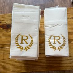 two white towels with gold monogrammed initials on them sitting on a wooden table