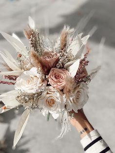 a bridal bouquet with feathers and flowers in someone's hand on the street