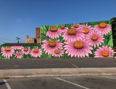 a large mural painted on the side of a building with pink flowers in front of it