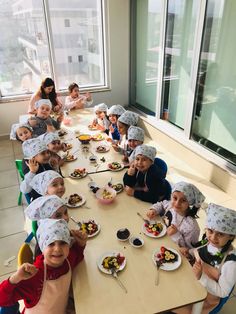 a group of children sitting at a table with hats on their heads eating some food