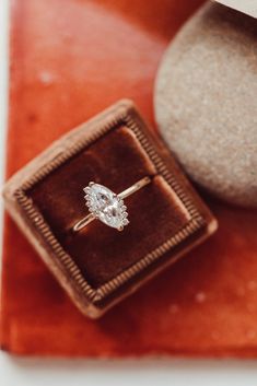 an engagement ring sitting on top of a velvet box next to a rock and stone