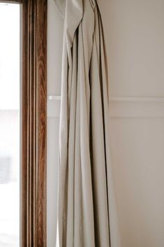 an open curtain hanging from the side of a window in a room with white walls and wood trim