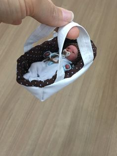 a hand is holding a small baby doll in a white and brown fabric bag on a wooden floor