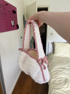 a hand holding a white crocheted purse in front of a bed with a pink headboard