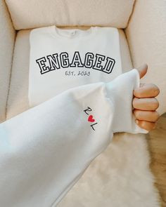 someone is holding up a white t - shirt with the word engaged on it and a red heart