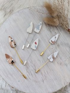 several different types of hair pins sitting on a table next to dried grass and feathers