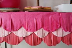 a pink table cloth with tassels on top of it next to plates and balloons