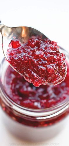 a spoon full of cranberry sauce on top of a glass bowl filled with jam