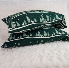 two green pillows with trees and deer on them sitting on a white furnishing