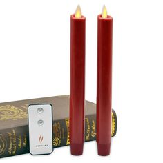 two red candles sitting on top of a book next to an electronic device and remote control