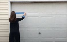 a woman is holding a tape in front of a garage door with her hand on the handle