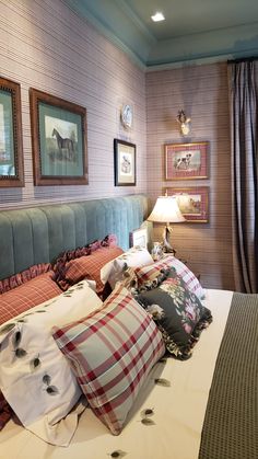 a bed with lots of pillows on top of it in a bedroom next to two framed pictures