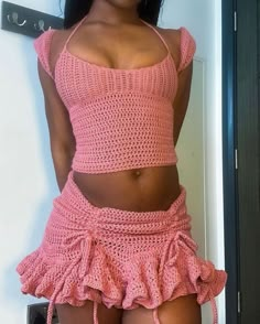 a woman wearing a pink crochet top and skirt