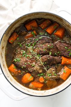 a pot filled with meat and carrots on top of a table