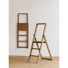 an easel leaning against a wall next to a wooden ladder on the floor in front of a white wall