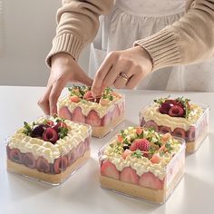 a woman placing strawberries on top of desserts in small square pans,