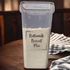 a plastic container filled with buttermilk sitting on top of a wooden table next to a towel