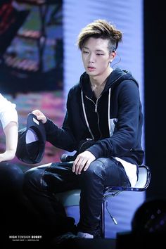 a man sitting on top of a white chair next to another person wearing a black hoodie