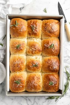 freshly baked garlic bread rolls in a baking pan with rosemary sprigs