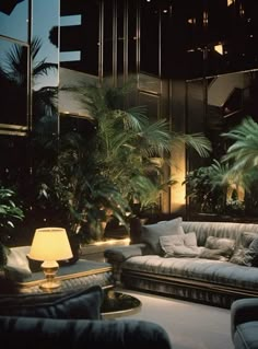 a living room filled with lots of furniture next to palm trees and windows at night