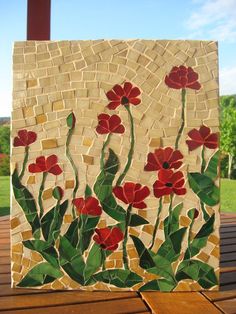 a painting with red flowers on it sitting on top of a wooden table next to grass