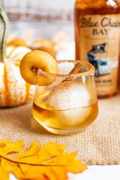 a glass filled with liquid and a donut on top of it next to some fall leaves