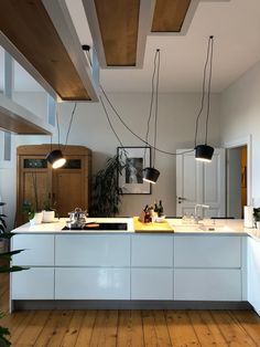 a kitchen with wooden flooring and white counter tops, hanging lights above the island